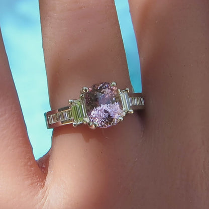 Close up of light pink sapphire cushion cut ring with baguette diamonds on either side shown on the hand