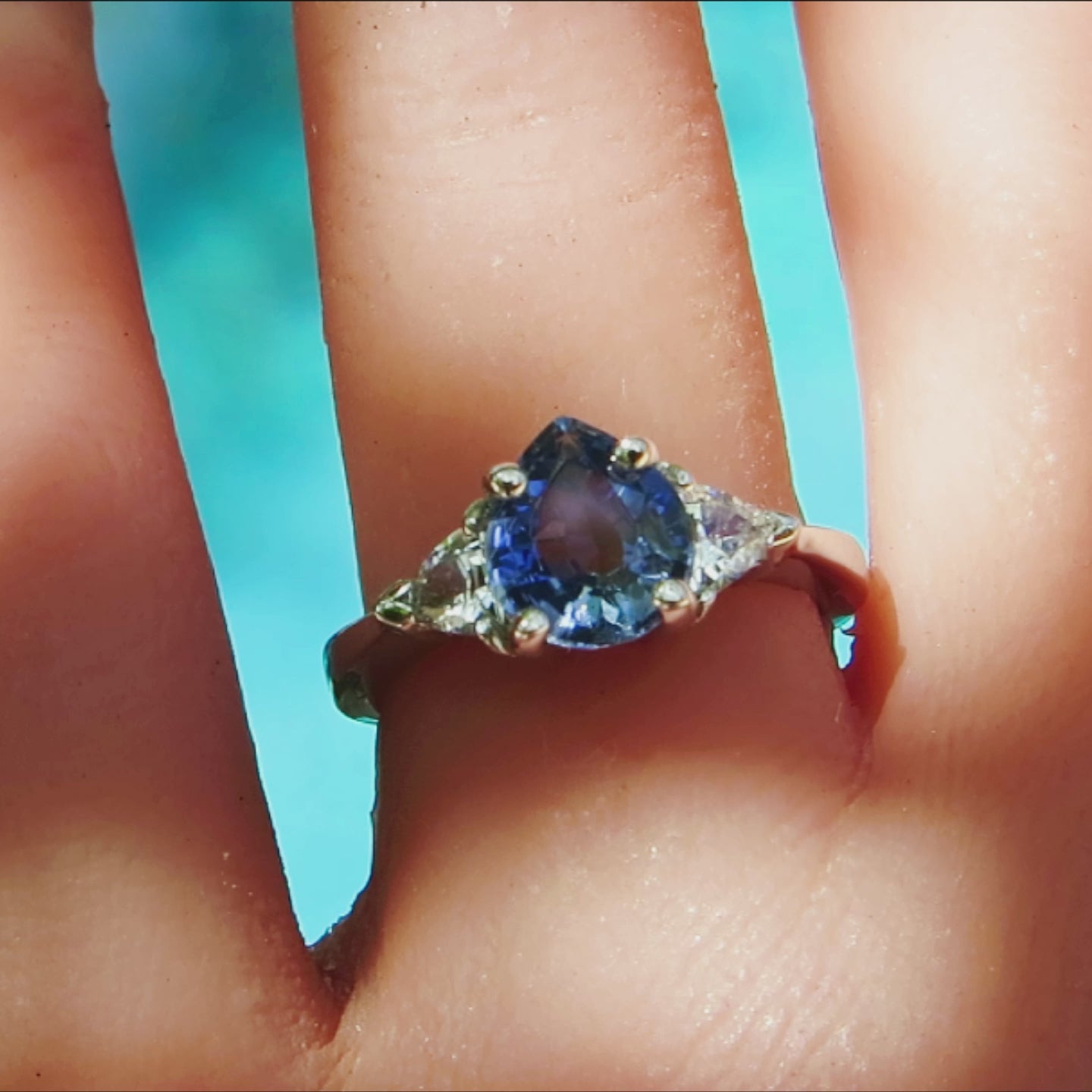 past present future 3 stone ring with pear cut blue sapphire and trillion white sapphires in a white metal 14k on the hand