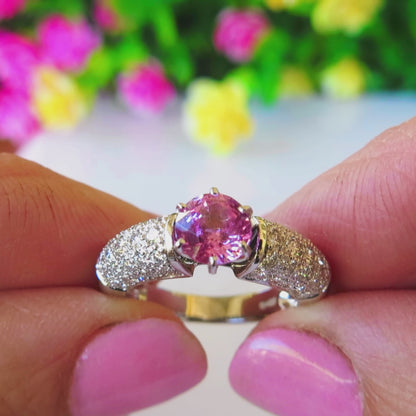 pave diamond ring with center round pink sapphire in 6 prong setting held by ladies' fingers 