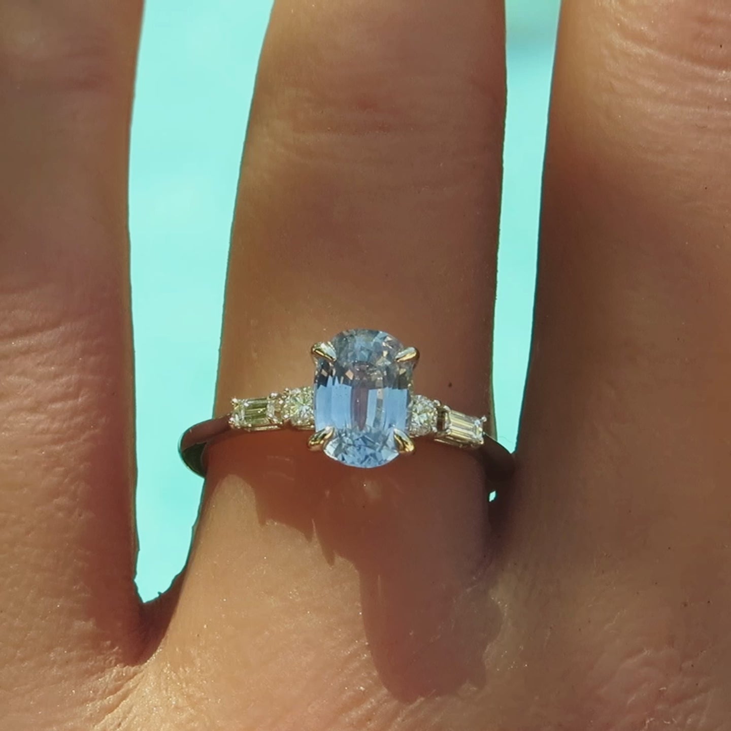 Pastel oval sapphire flanked by round and baguette clear diamonds in a skinny band on the finger