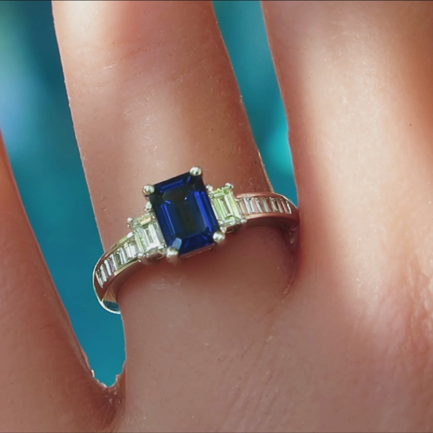 rectangular emerald cut blue sapphire with large and small baguette diamonds on either side in white gold on the finger
