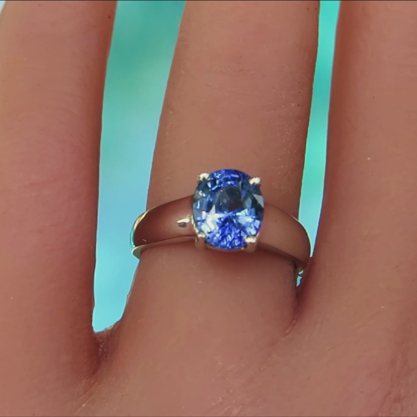 oval sapphire solitaire ring in white metal show on ladies hand with blue background