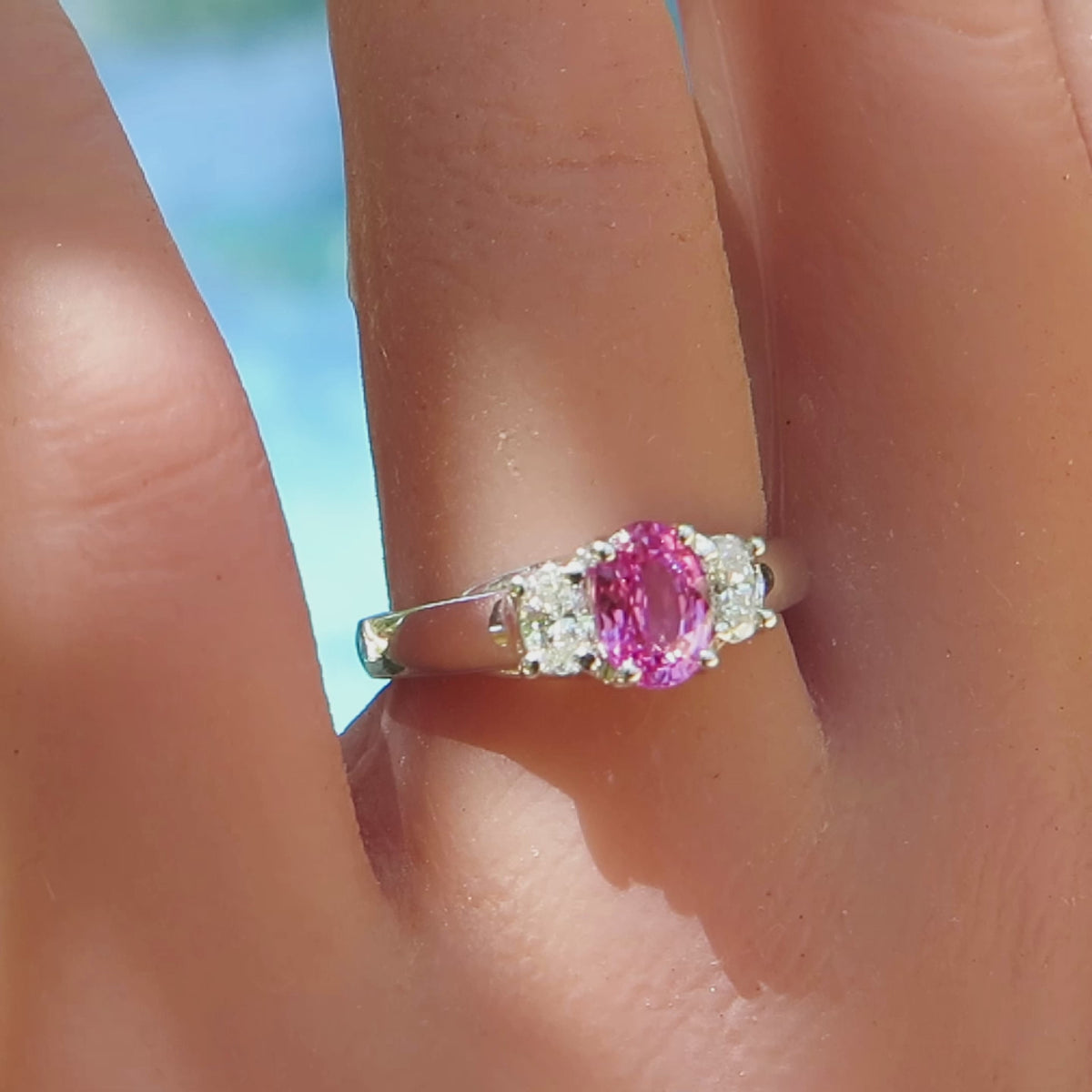 close up of three stone pink sapphire and diamond ring with oval stones in white gold on the finger