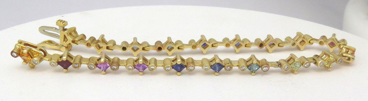 A yellow gold chain bracelet with small star-shaped links and alternating round diamonds and square sapphires in blue, purple, and green, displayed on a white surface.