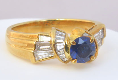 A yellow gold ring featuring a round blue sapphire center stone and baguette-cut clear stones on the shoulders, shown on a plain light background.