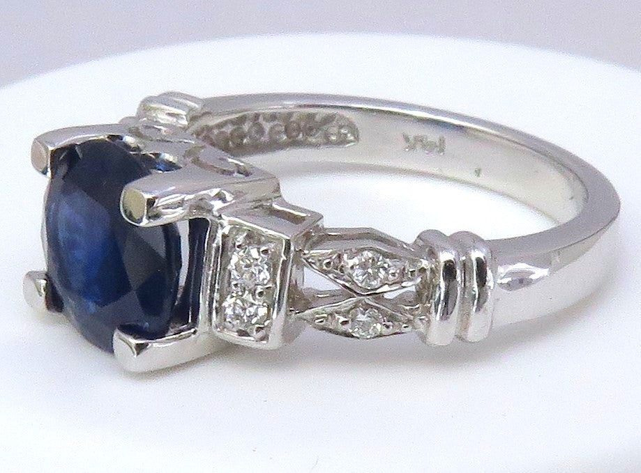 A white gold ring featuring a 8mm round cut dark blue sapphire center stone and small clear accent diamonds, shown on a plain white background.