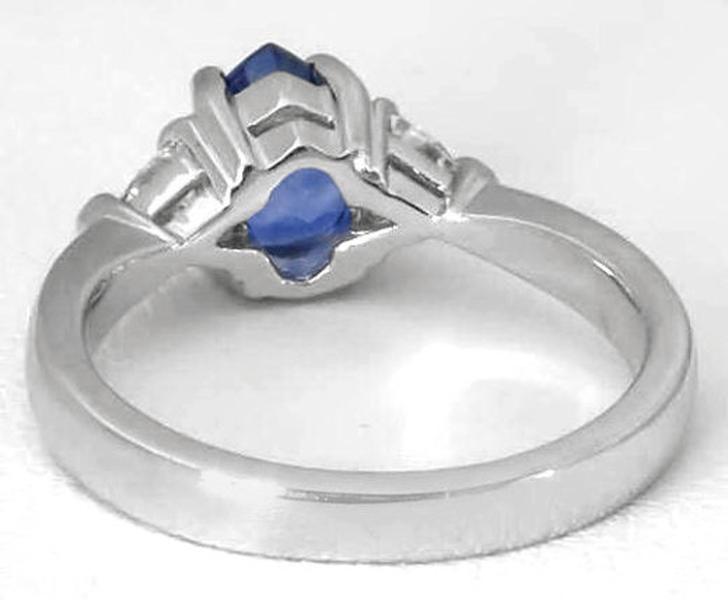 A silver-colored ring featuring a central marquise-cut blue gemstone and smaller side stones, shown on a plain light background.