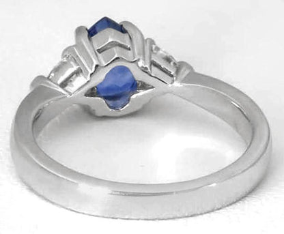 A silver-colored ring featuring a central marquise-cut blue gemstone and smaller side stones, shown on a plain light background.