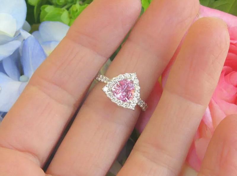 Natural trillion cut pink sapphire ring with a diamond halo in 14k white gold shown on the finger for scale