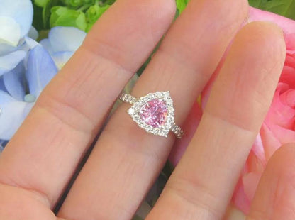 Natural trillion cut pink sapphire ring with a diamond halo in 14k white gold shown on the finger for scale