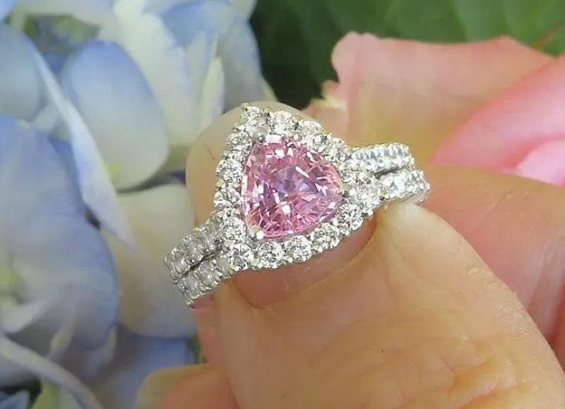 Natural trillion cut pink sapphire ring with a diamond halo in 14k white gold shown with it's matching diamond band in a natural setting held in the hand