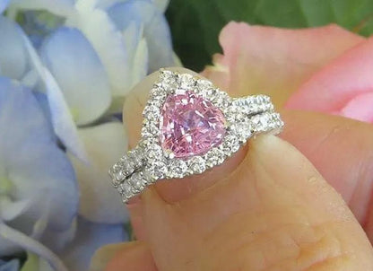 Natural trillion cut pink sapphire ring with a diamond halo in 14k white gold shown with it's matching diamond band in a natural setting held in the hand