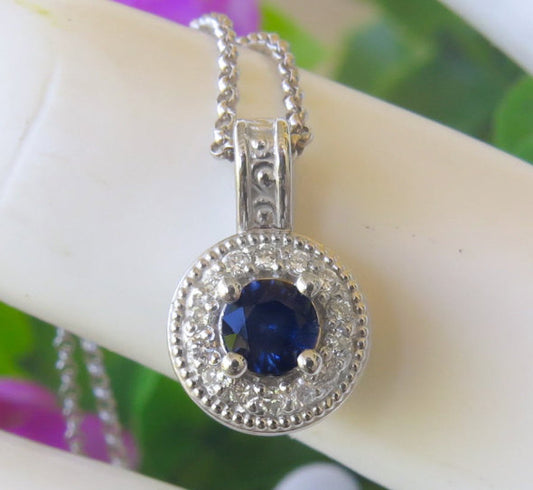 Round blue sapphire and diamond halo pendant in white gold, featuring a vivid blue center sapphire surrounded by sparkling diamonds.