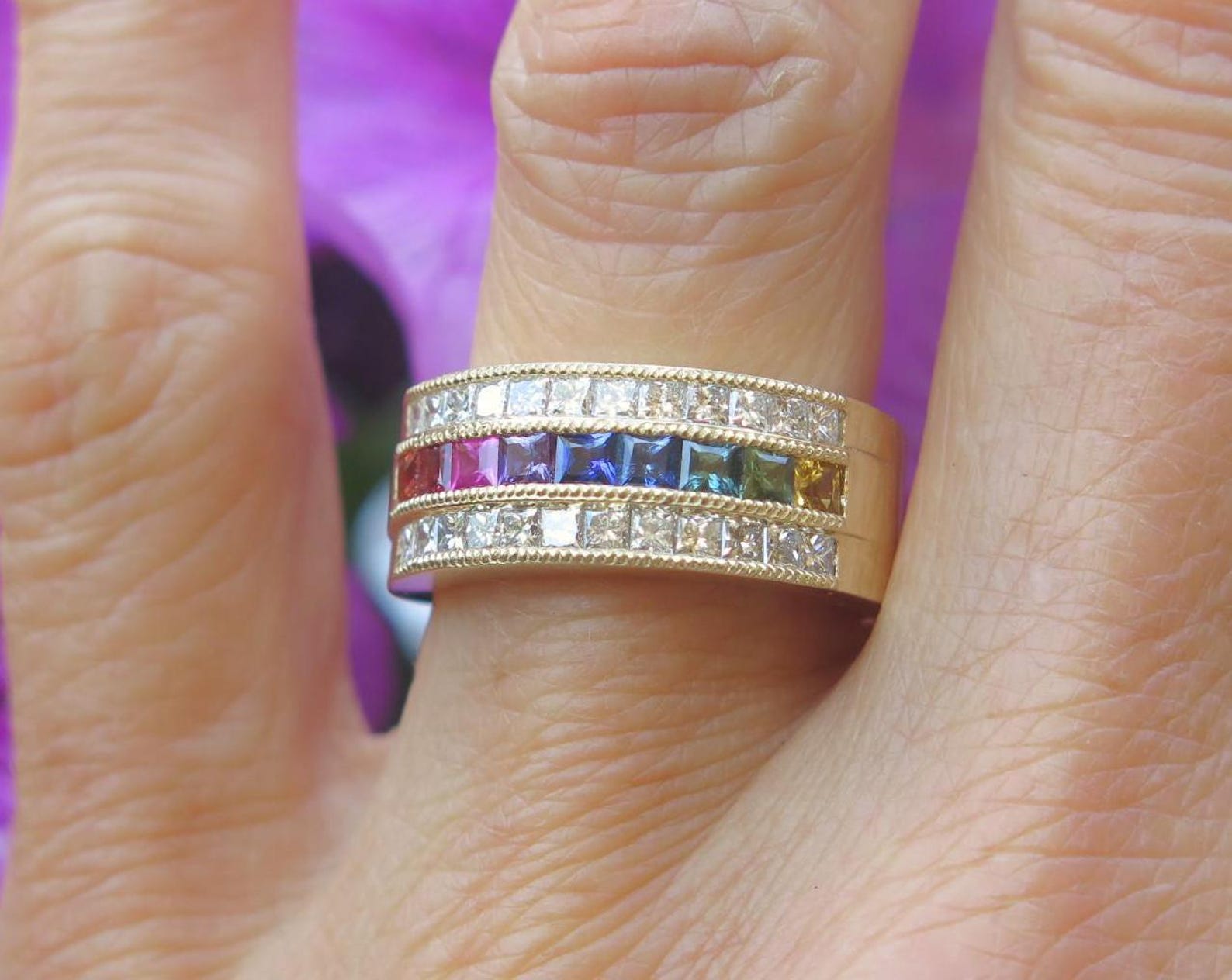 close up of natural rainbow sapphire ring with princess cut gemstones on finger. Three fingers are showing.