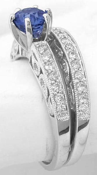 A white gold double-band ring set with a large oval-cut blue sapphire and pavé-set clear stones, shown on a white ring stand.